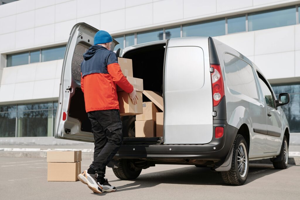 Man in colorful jacket loading cardboard boxes into a van outside an office building.